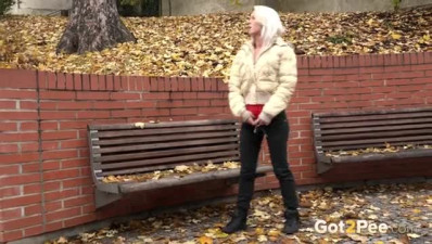 Desperate blonde pees in the leaves by a bench