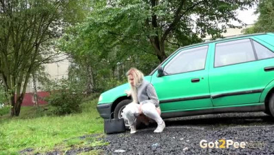 Sexy blonde babe hides behind a car to kneel down and take a long pee