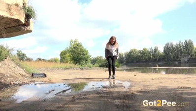 Sexy brunette teen in black pants squats down and pees in a puddle